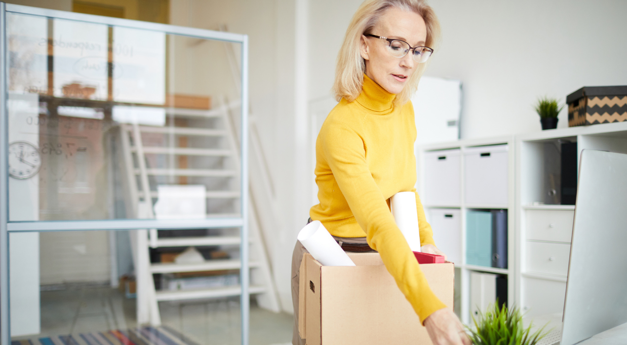 Blonde woman with glasses in turtleneck packing office supplies in office